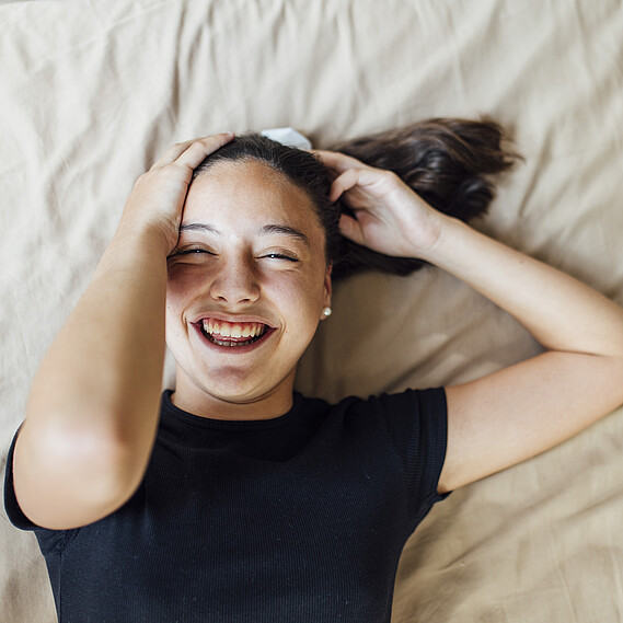 Pre-adolescent girl hands in hair lying on bed at home